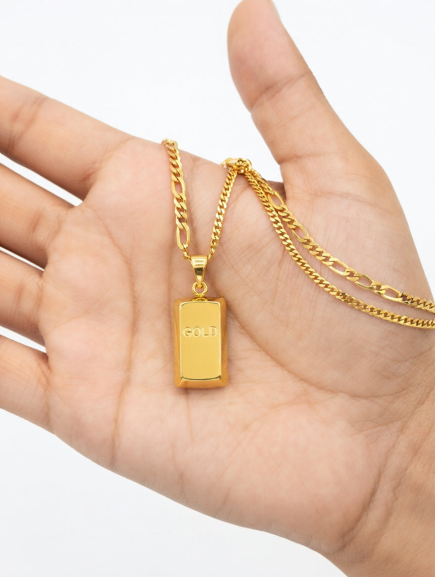 Gold bar pendant and Figaro chain necklace from Ashir Studio, showcasing elegant jewelry with polished gold finish.