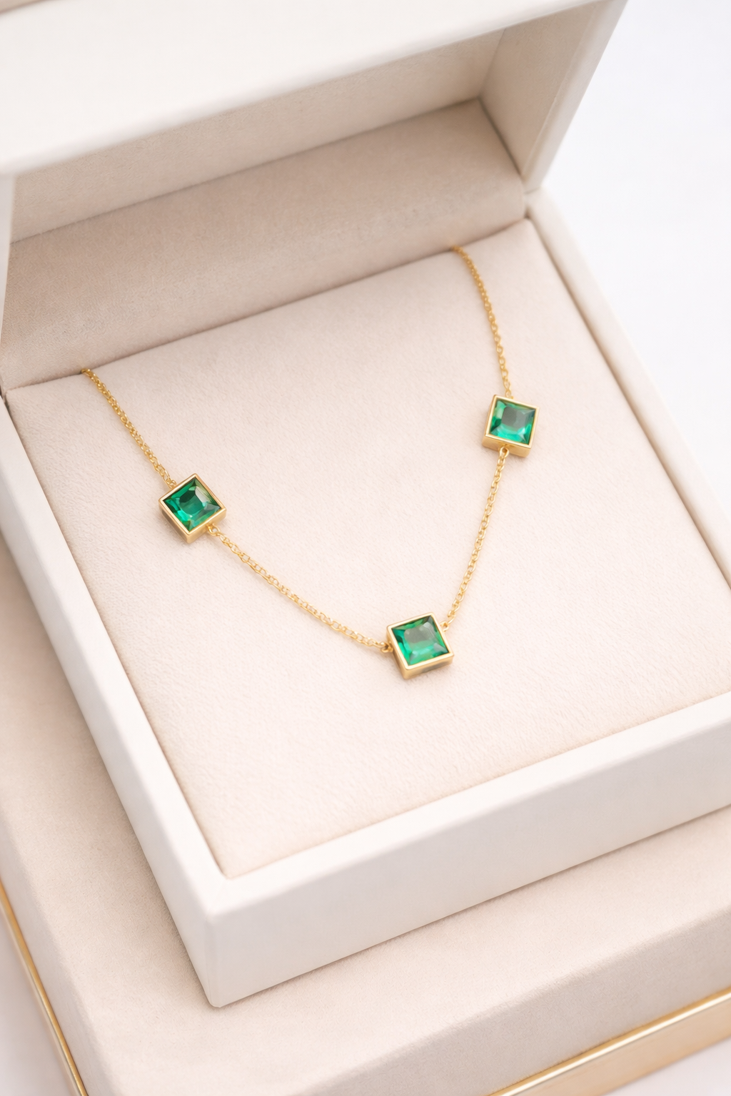 Elegant Golg plated emerald necklace by Ashir Studio featuring three vibrant emerald stones on a delicate jewelry chain.