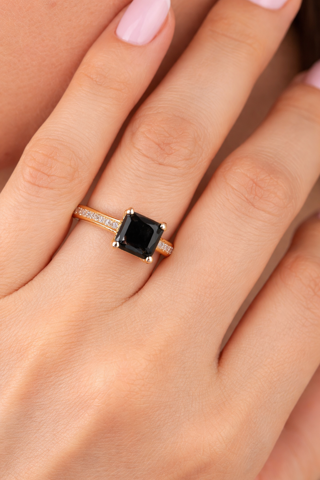 Hand wearing an Ashir Studio emerald-cut black diamond halo ring in 18K yellow gold, showcasing elegant jewelry design.